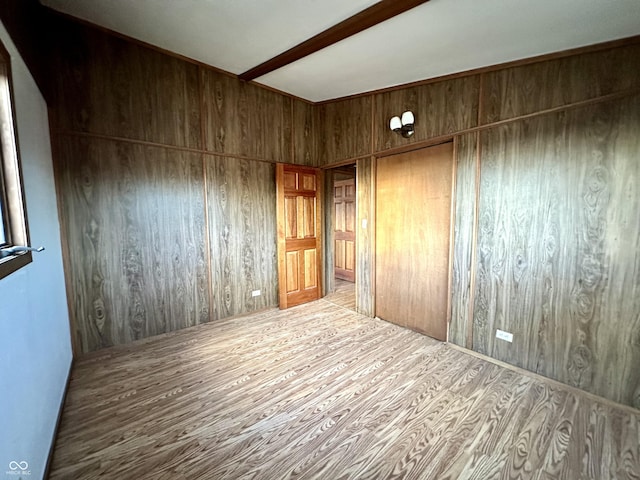 unfurnished room featuring wooden walls, wood finished floors, and beamed ceiling