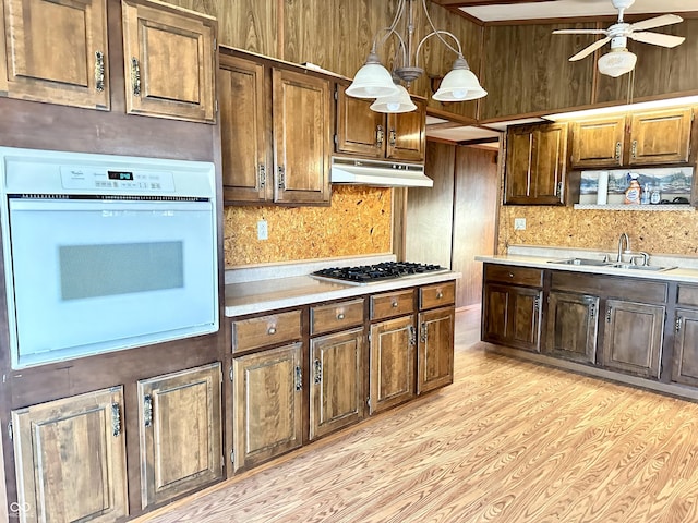 kitchen featuring oven, under cabinet range hood, a sink, stainless steel gas stovetop, and light countertops