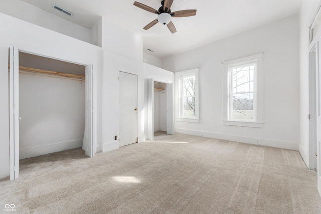 unfurnished bedroom featuring carpet, two closets, visible vents, and baseboards