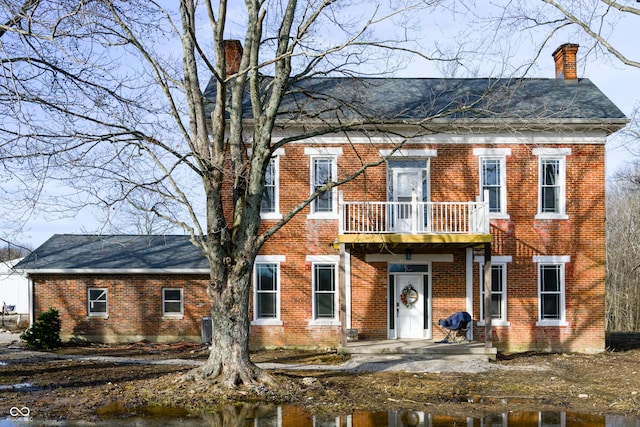 view of front of home with central AC, brick siding, a chimney, and a balcony