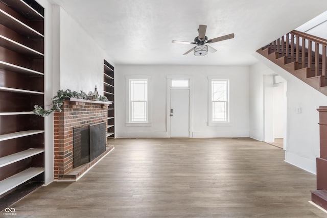 unfurnished living room featuring a ceiling fan, a brick fireplace, stairway, and wood finished floors