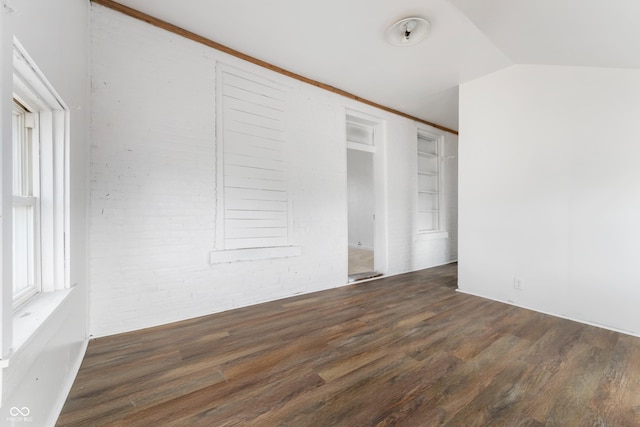 spare room with vaulted ceiling, brick wall, and wood finished floors