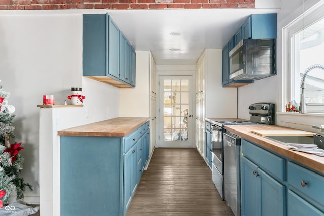 kitchen with blue cabinets, butcher block counters, stainless steel appliances, and dark wood-style flooring