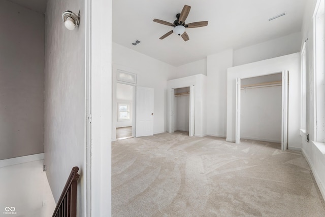 unfurnished bedroom with a ceiling fan, two closets, visible vents, and light colored carpet