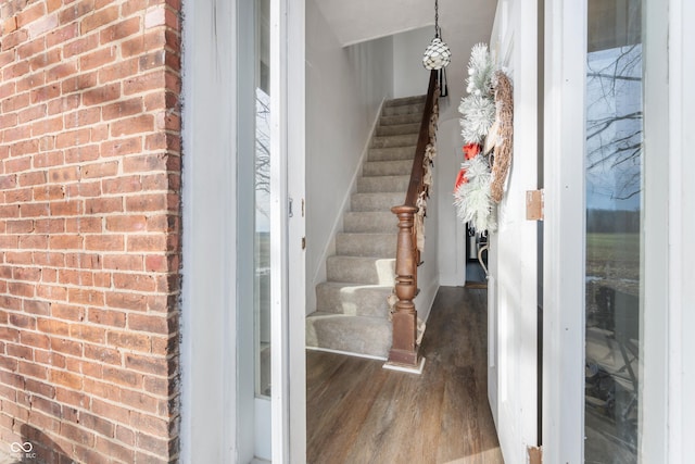 entrance foyer with stairs, brick wall, and wood finished floors