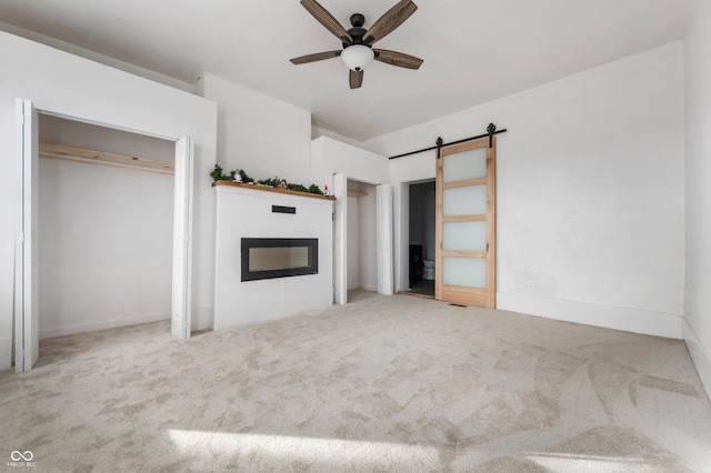 unfurnished bedroom with a barn door, carpet, a glass covered fireplace, and visible vents