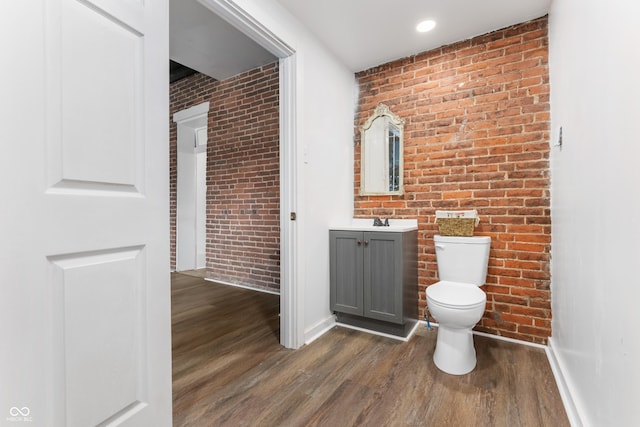 half bath featuring baseboards, toilet, brick wall, wood finished floors, and vanity