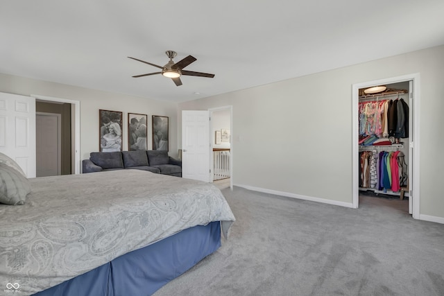 carpeted bedroom with a ceiling fan, a walk in closet, a closet, and baseboards