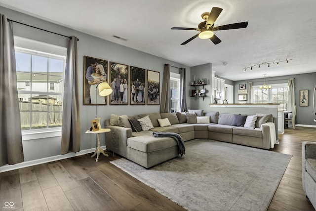 living room with ceiling fan with notable chandelier, wood finished floors, visible vents, baseboards, and track lighting