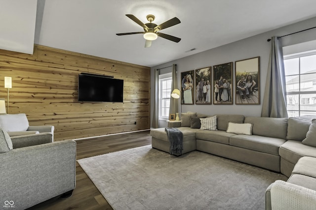 living area with dark wood-style floors, wooden walls, and a ceiling fan