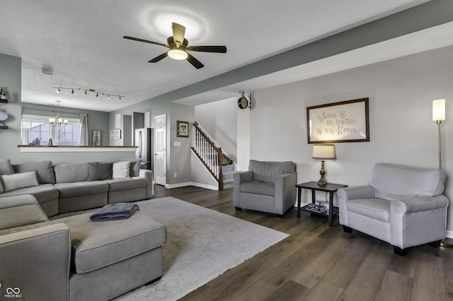 living area featuring dark wood-type flooring, ceiling fan with notable chandelier, baseboards, and stairs