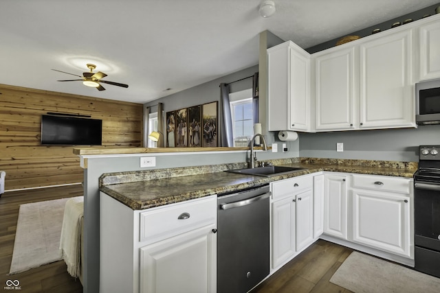 kitchen with dark wood-style flooring, stainless steel appliances, a sink, wood walls, and a peninsula