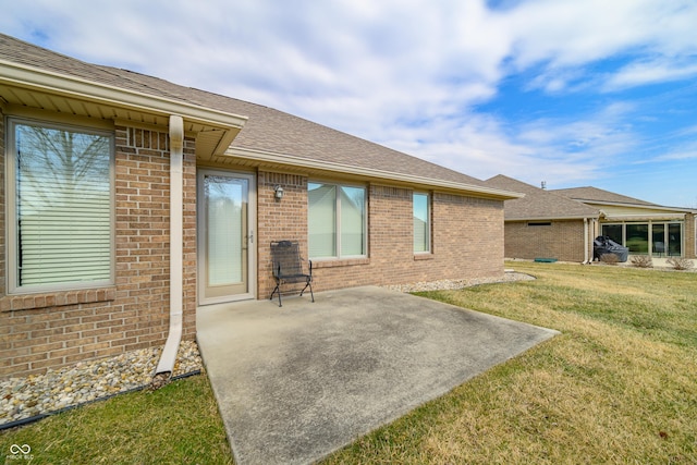 back of house with a yard, brick siding, a patio area, and a shingled roof