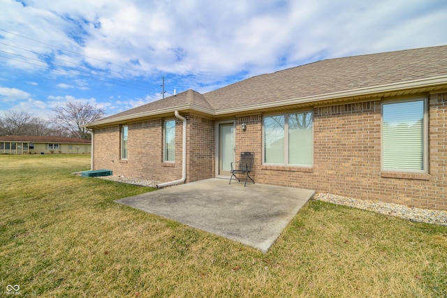 rear view of house with brick siding, roof with shingles, a lawn, and a patio