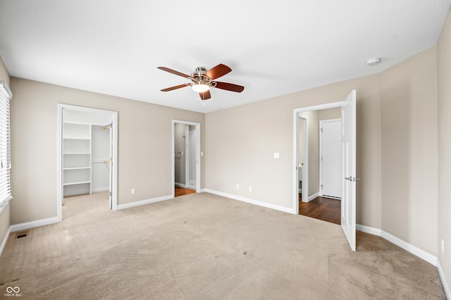 unfurnished bedroom with carpet, visible vents, a spacious closet, ceiling fan, and baseboards