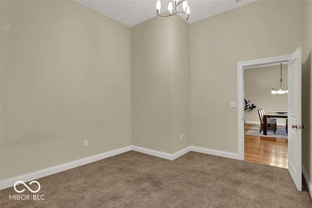 carpeted empty room featuring a chandelier and baseboards