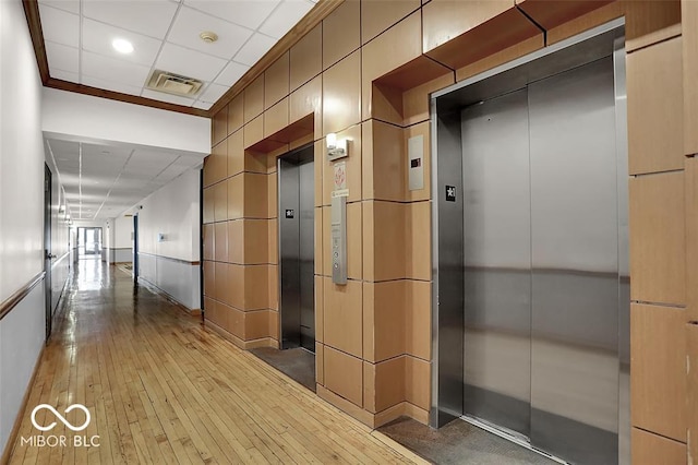 corridor featuring hardwood / wood-style flooring, elevator, visible vents, and a drop ceiling