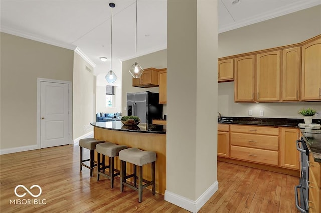 kitchen with stainless steel fridge, dark countertops, crown molding, light wood-style floors, and a kitchen bar