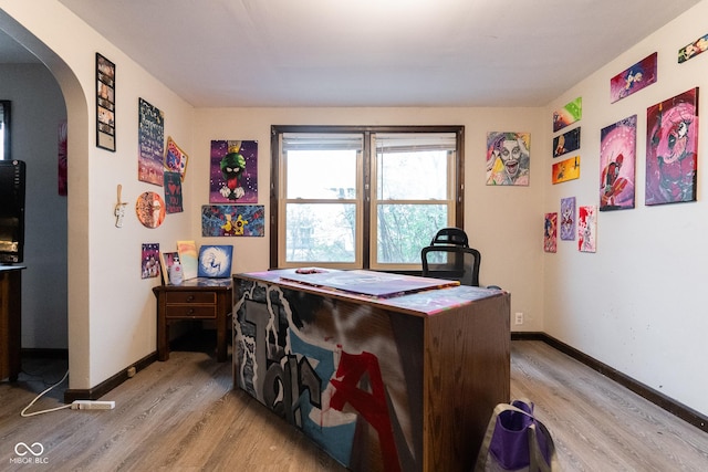 office area with arched walkways, baseboards, and light wood finished floors