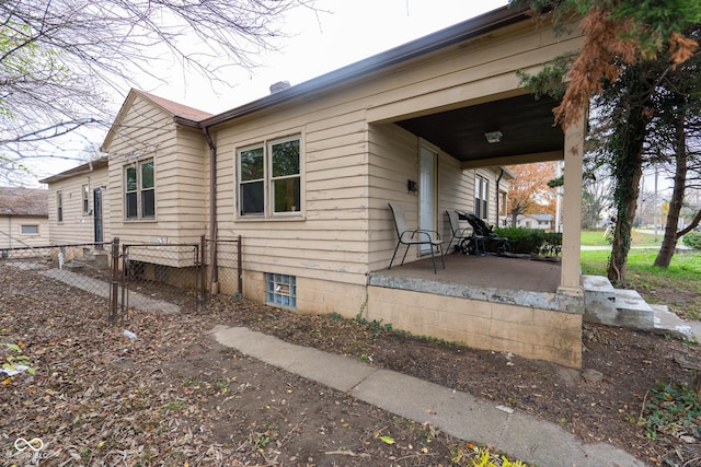 view of side of property featuring covered porch, a chimney, and fence