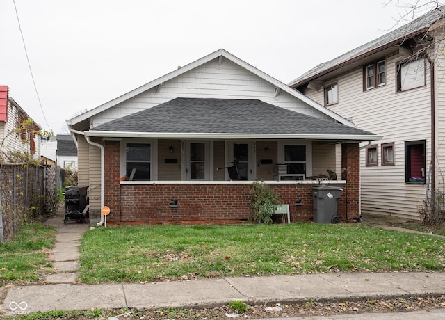 bungalow-style home featuring brick siding, a shingled roof, covered porch, a front yard, and fence