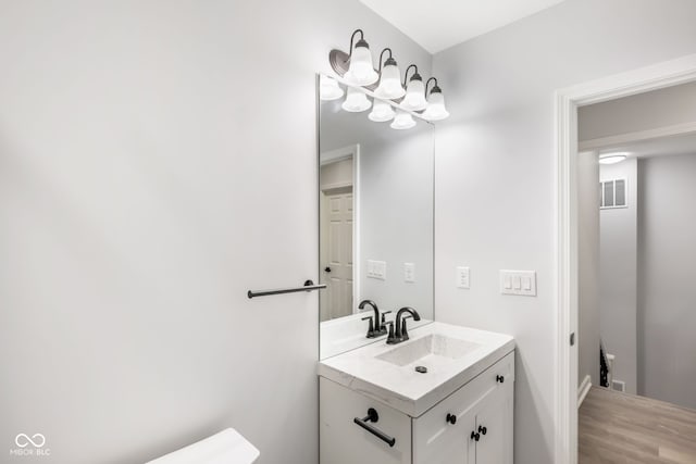 half bath with toilet, visible vents, wood finished floors, and vanity