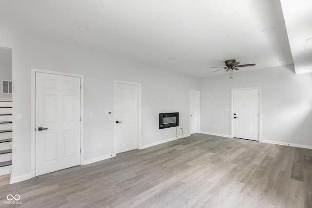 unfurnished living room with ceiling fan, baseboards, wood finished floors, and a glass covered fireplace