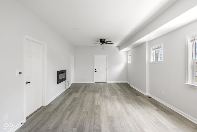 unfurnished living room with heating unit, a ceiling fan, a glass covered fireplace, wood finished floors, and baseboards