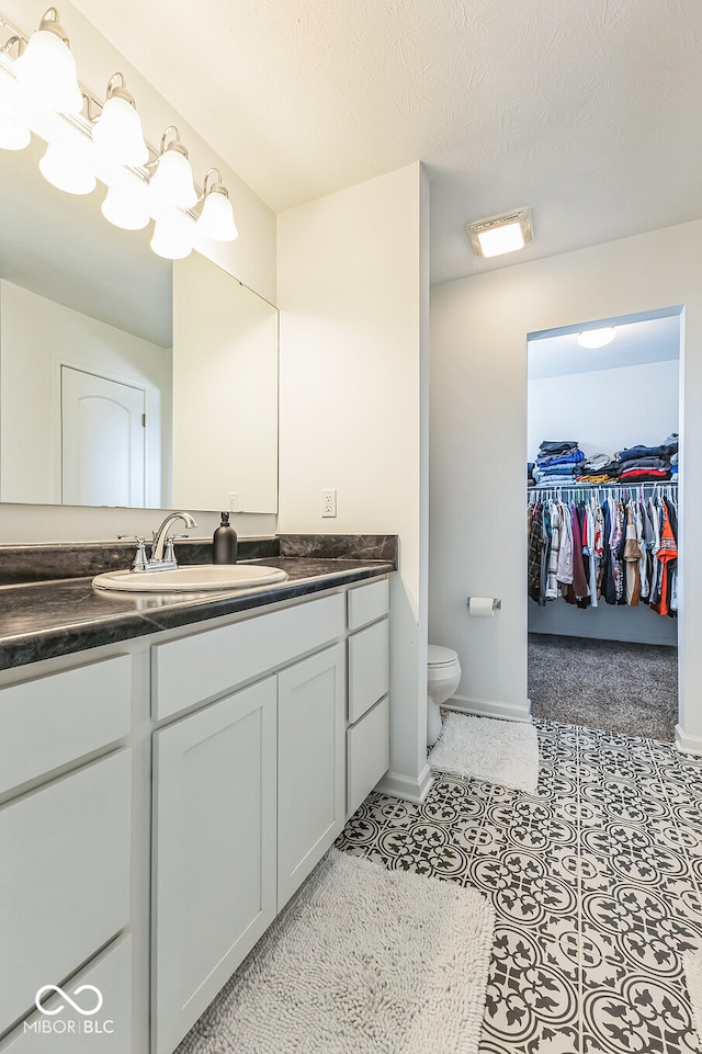 bathroom with a spacious closet, toilet, a textured ceiling, vanity, and baseboards