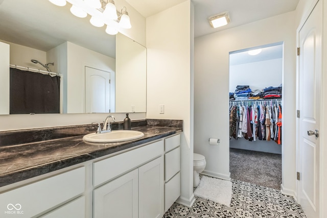 bathroom with toilet, vanity, baseboards, tile patterned floors, and a walk in closet