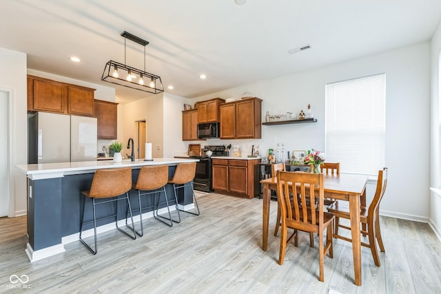 kitchen with a sink, visible vents, brown cabinets, black appliances, and an island with sink