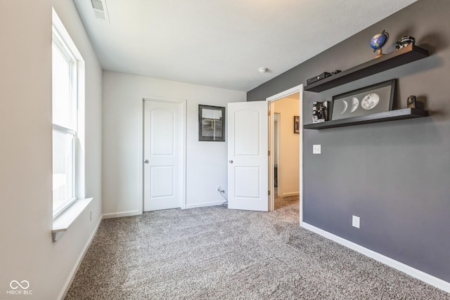 unfurnished bedroom featuring carpet floors, multiple windows, visible vents, and baseboards