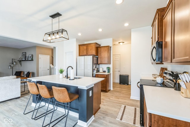 kitchen featuring a kitchen bar, light wood-style flooring, brown cabinetry, a sink, and black appliances