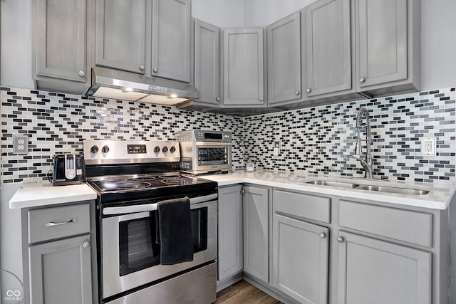 kitchen featuring electric range, a sink, gray cabinetry, under cabinet range hood, and backsplash