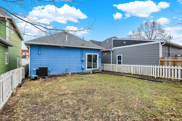 back of property with central air condition unit, a fenced backyard, roof with shingles, and a yard