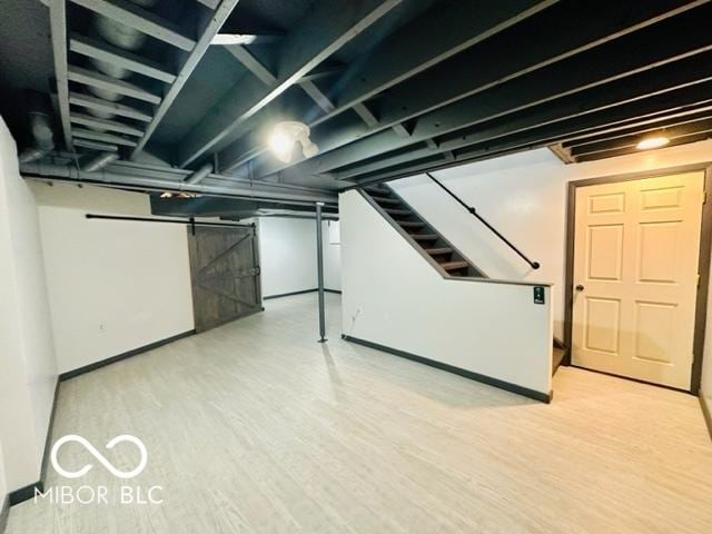 finished basement with a barn door, stairway, and wood finished floors