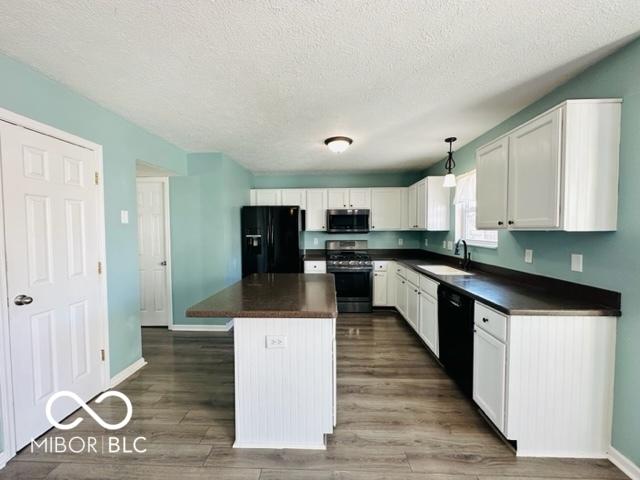 kitchen with black appliances, a kitchen island, dark countertops, and a sink