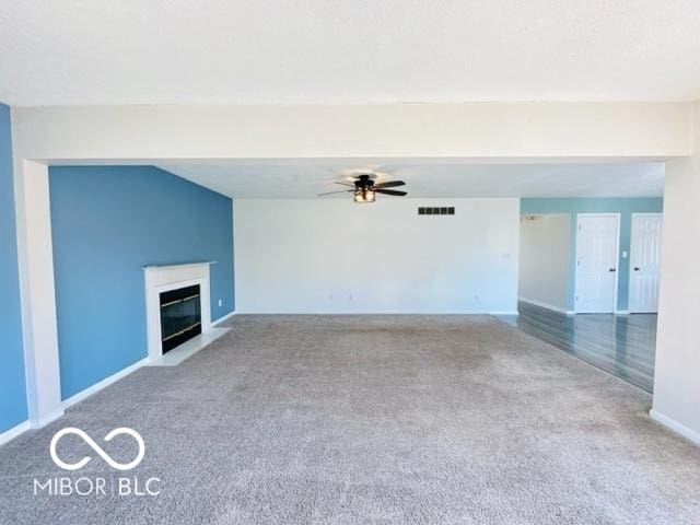 unfurnished living room featuring ceiling fan, carpet flooring, a fireplace with flush hearth, visible vents, and baseboards