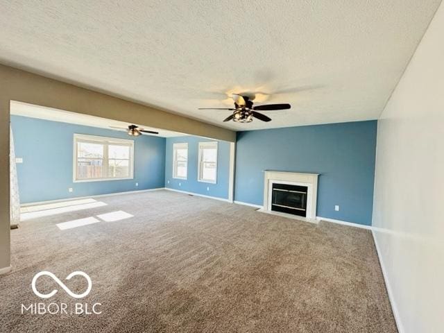 unfurnished living room with a textured ceiling, carpet floors, a fireplace with flush hearth, and baseboards