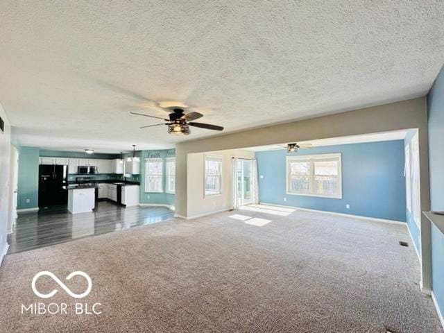 unfurnished living room with a ceiling fan, dark carpet, a textured ceiling, and baseboards