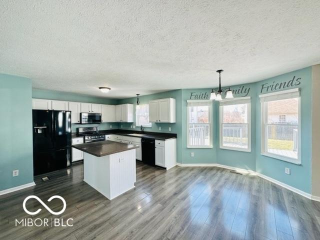 kitchen with dark wood-style floors, dark countertops, white cabinets, a sink, and black appliances