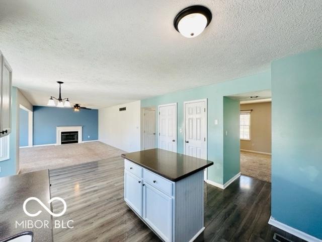 kitchen featuring a kitchen island, white cabinetry, open floor plan, dark countertops, and dark wood finished floors