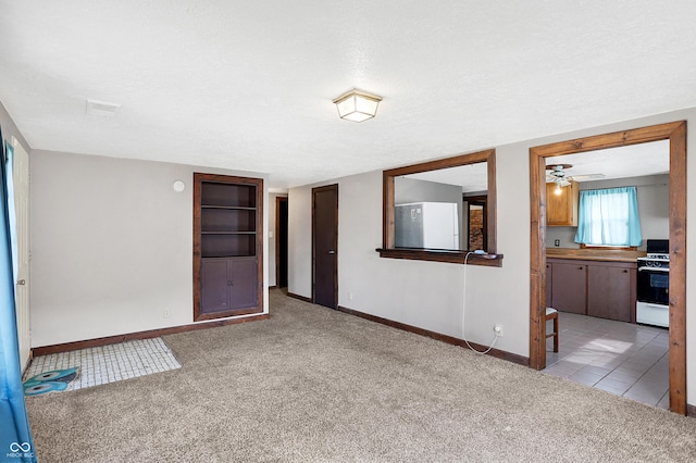 spare room featuring light carpet, light tile patterned floors, a textured ceiling, and baseboards