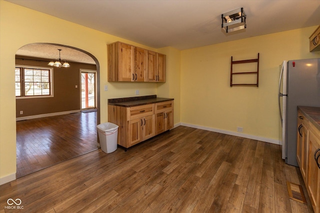 kitchen featuring arched walkways, freestanding refrigerator, dark countertops, dark wood finished floors, and an inviting chandelier