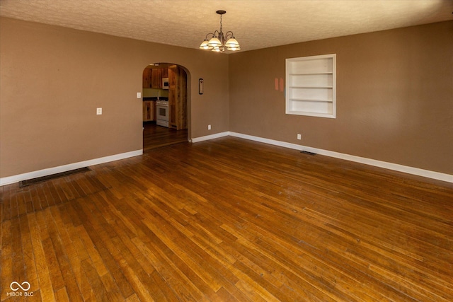 unfurnished room featuring arched walkways, a textured ceiling, baseboards, built in features, and dark wood-style floors