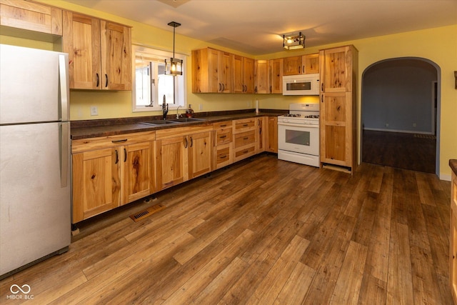 kitchen featuring white appliances, dark wood-type flooring, dark countertops, and a sink