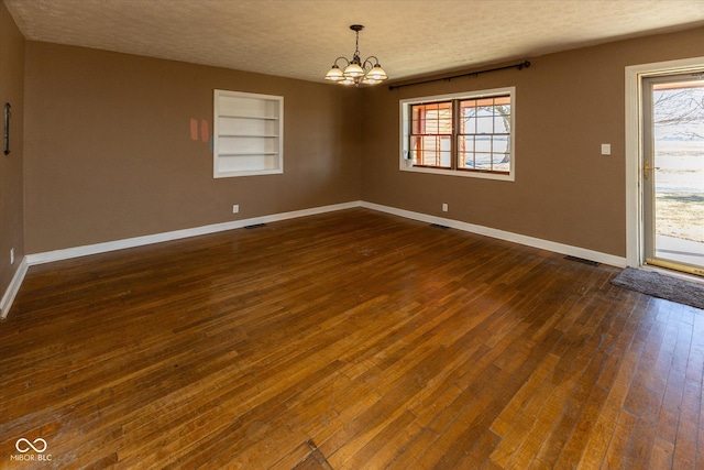 empty room featuring a healthy amount of sunlight, a textured ceiling, baseboards, and dark wood-type flooring