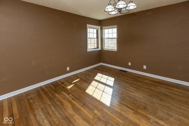 unfurnished room featuring baseboards, visible vents, dark wood finished floors, and a chandelier