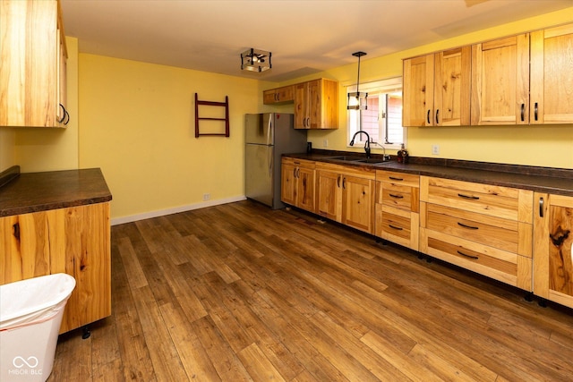 kitchen with dark wood finished floors, dark countertops, freestanding refrigerator, a sink, and baseboards