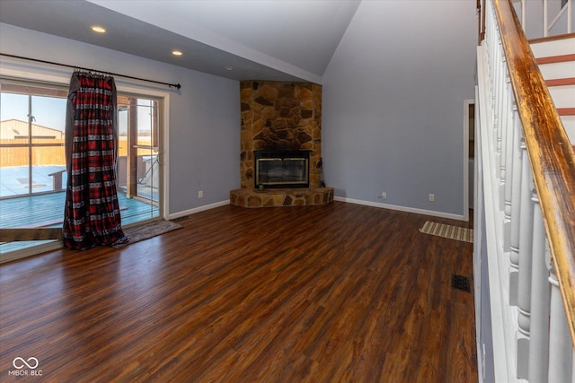 unfurnished living room featuring vaulted ceiling, a stone fireplace, baseboards, and wood finished floors